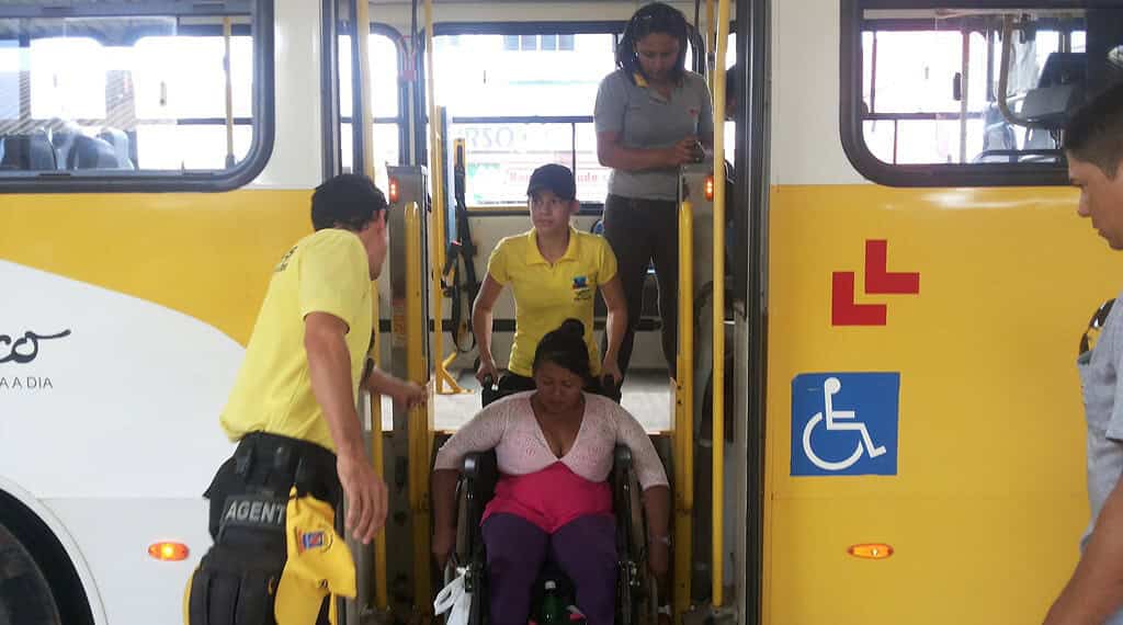 Cadeirante é auxiliada por agentes, na descida de ônibus