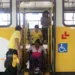 Cadeirante é auxiliada por agentes, na descida de ônibus