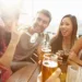 Group Of Friends Enjoying Drink At Outdoor Rooftop Bar Laughing And Chatting Around Table.