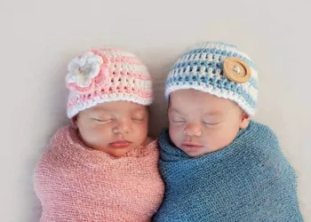 Five week old sleeping boy and girl fraternal twin newborn babies. They are wearing crocheted pink and blue striped hats.