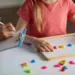 Unrecognizable little girl exercising with alphabet board during session with female child development specialist at clinic, small kid making words from colorful plastic letters, cropped image