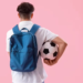 Male student with backpack and soccer ball on pink background, back view