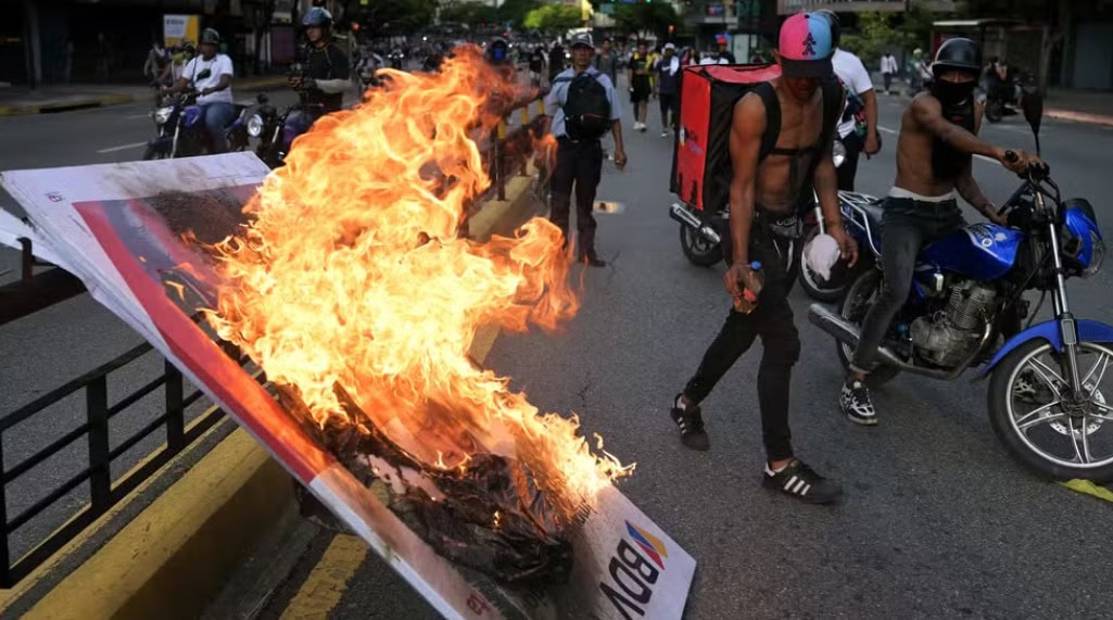 Manifestantes queimam banner durante protesto em Caracas, no dia 30 de julho de 2024, um dia após a eleição presidencial na Venezuela — Foto: Yuri Cortez/AFP