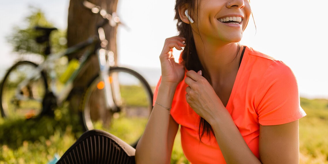 portrait of smiling beautiful woman doing sports in morning in park nature on mat wearing colorful fitness outfit, happy healthy lifestyle, music in earphones, bicycle on background