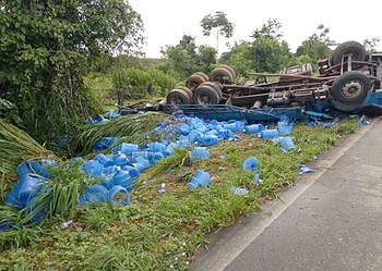Motorista é resgatado após caminhão com galões de água capotar na BR-364