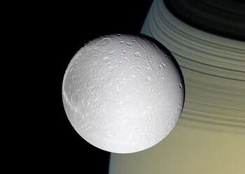 Dione, uma das agora 274 luas de Saturno, vista com Saturno e seus anéis ao fundo: novas descobertas consolidam o lugar de Saturno como o vencedor da competição de número luas no Sistema Solar, com mais luas confirmadas do que todos os outros planetas juntos. — Foto: NASA / JPL / Space Science Institute